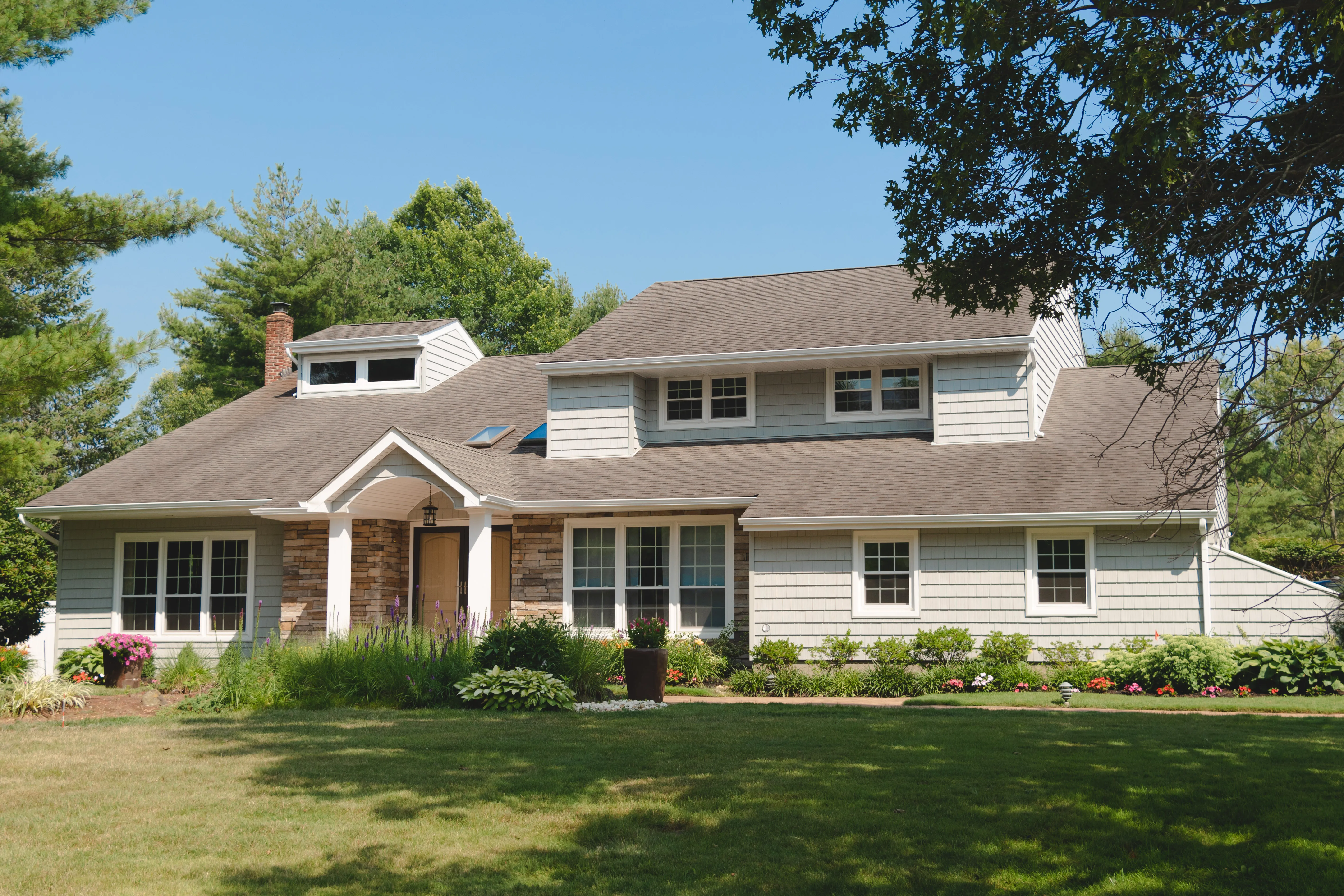 Large cape cod home with tan vinyl siding and stone veneer accent around the front entry portico