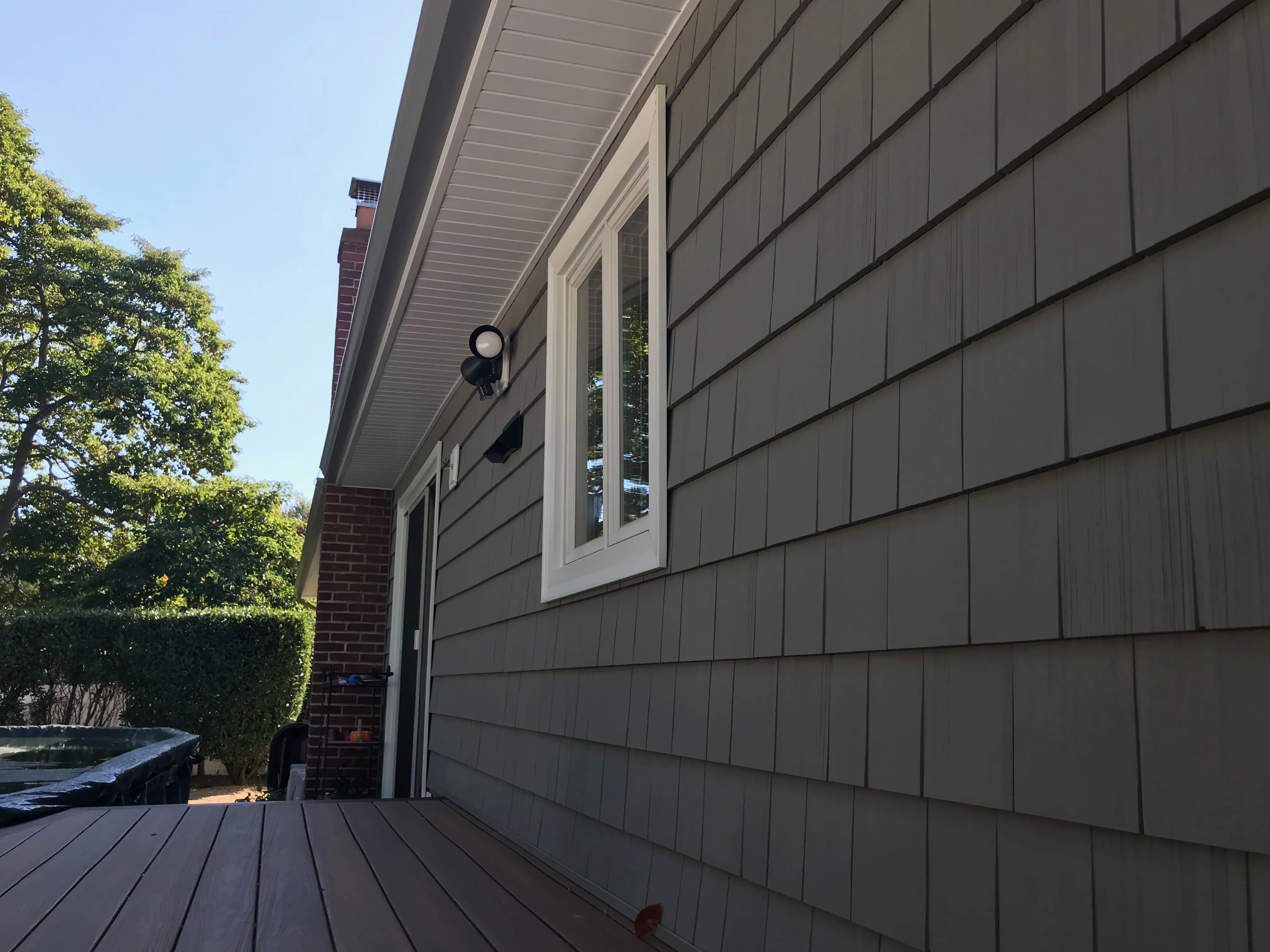 Side view of a home with olive-green shake-style siding, white soffit and fascia, and composite deck