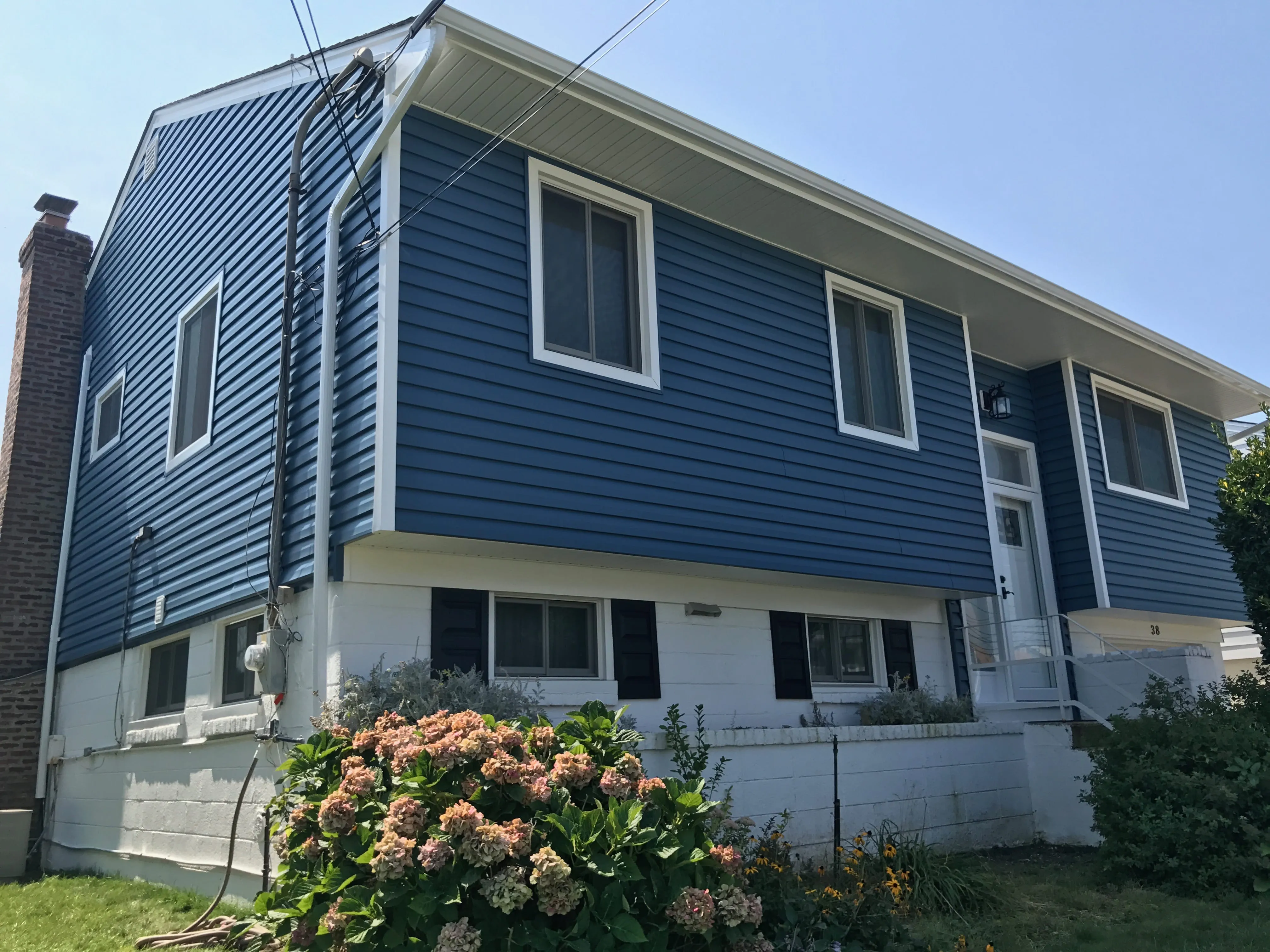 Two-story home with bright blue horizontal vinyl siding, white trim, and hydrangea bushes