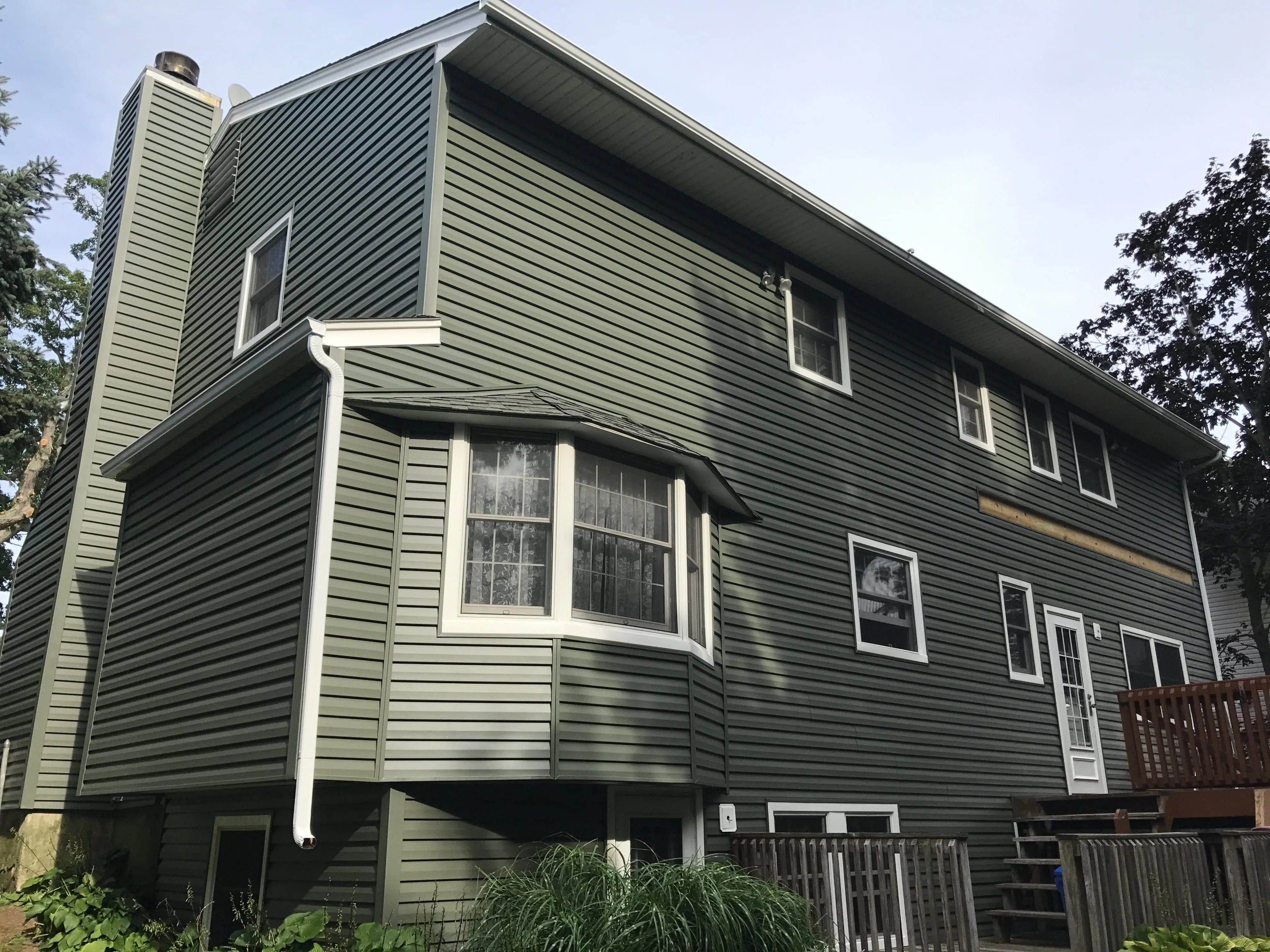 Two-story home with dark green horizontal vinyl siding, white trim, and bay window
