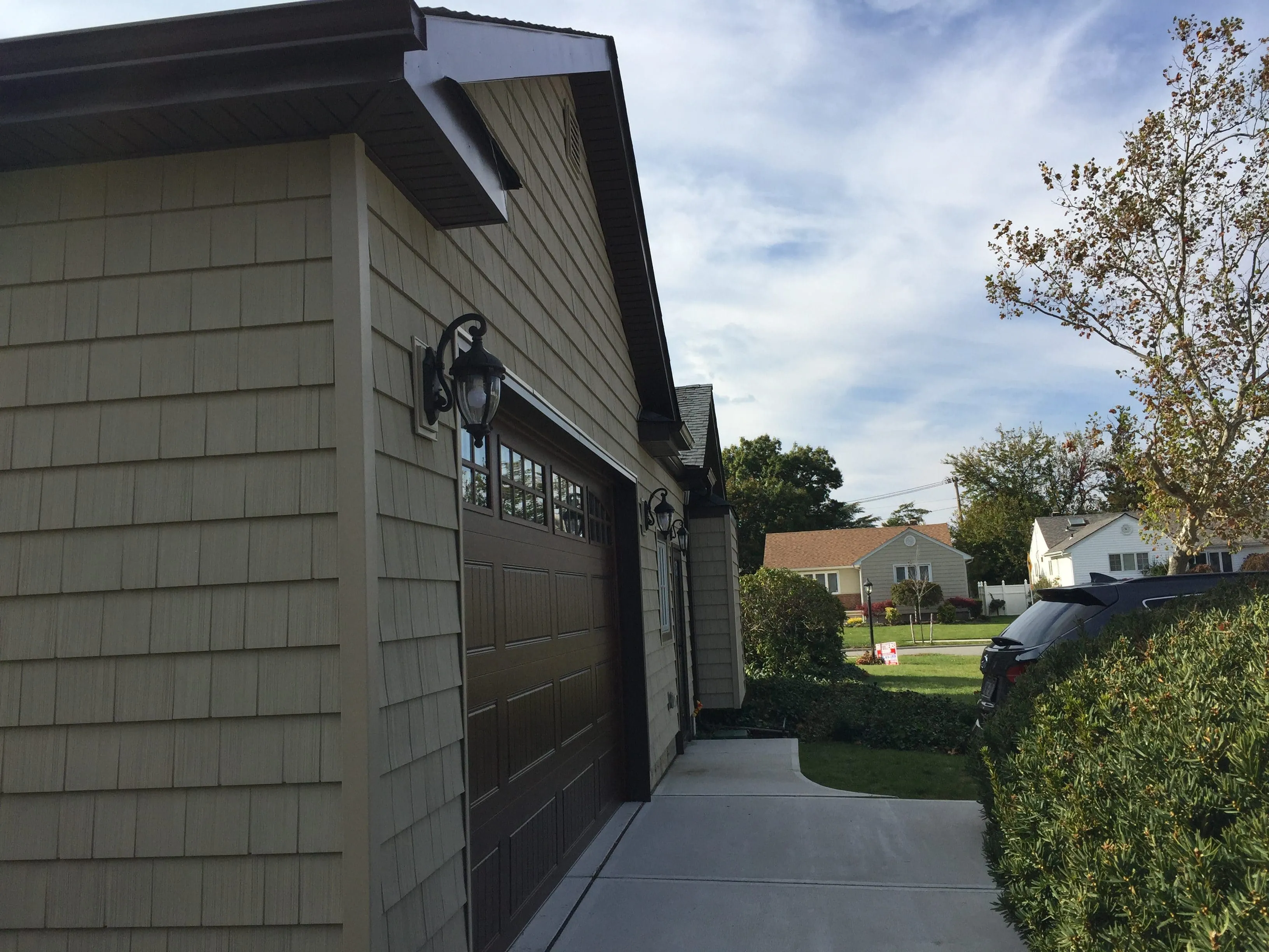 Attached garage with tan shake-style vinyl siding, glass-panel garage door, and decorative sconce light