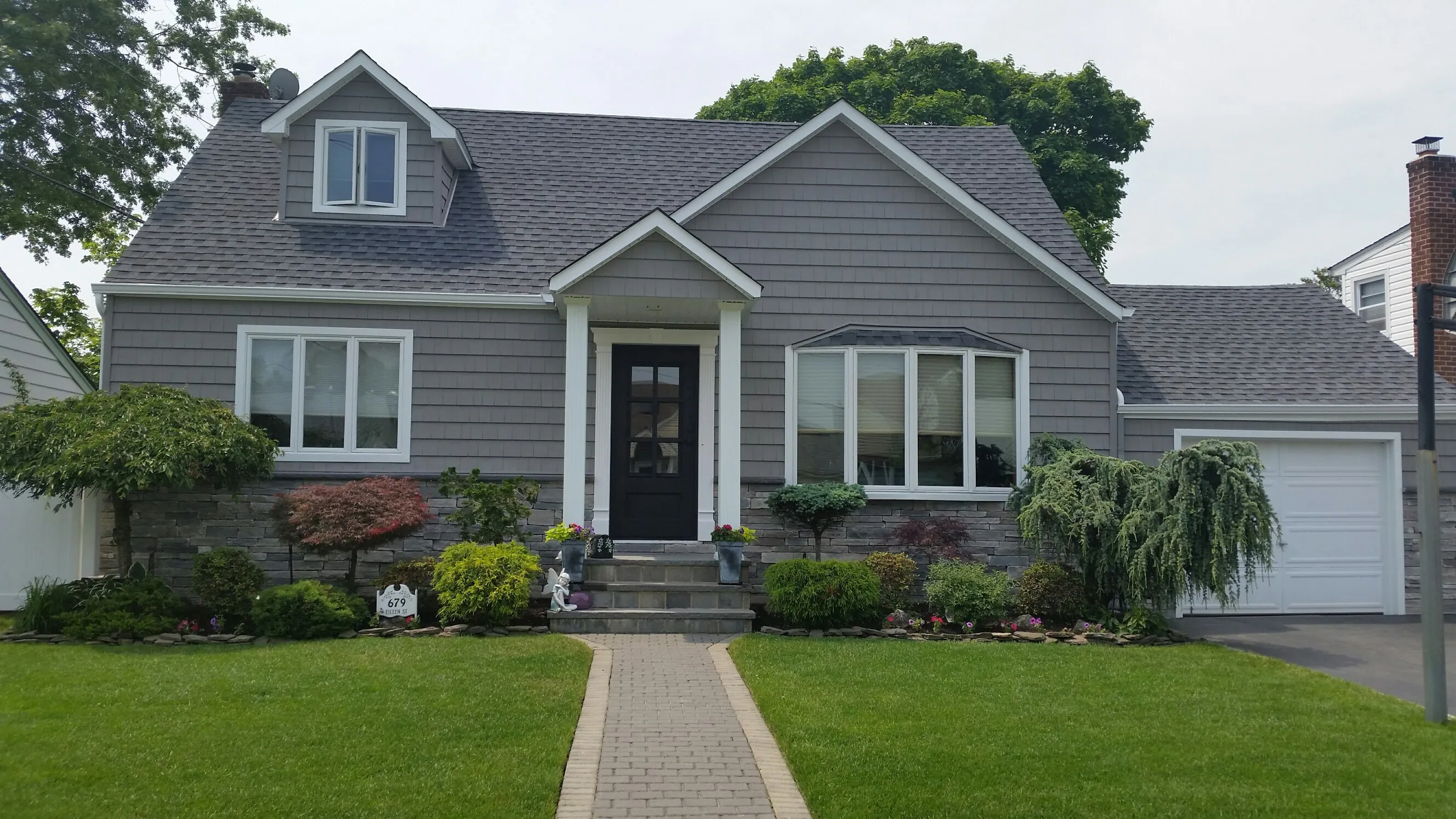 Gray cape cod with horizontal vinyl siding, shake gable accents, stone veneer foundation, and brick walkway