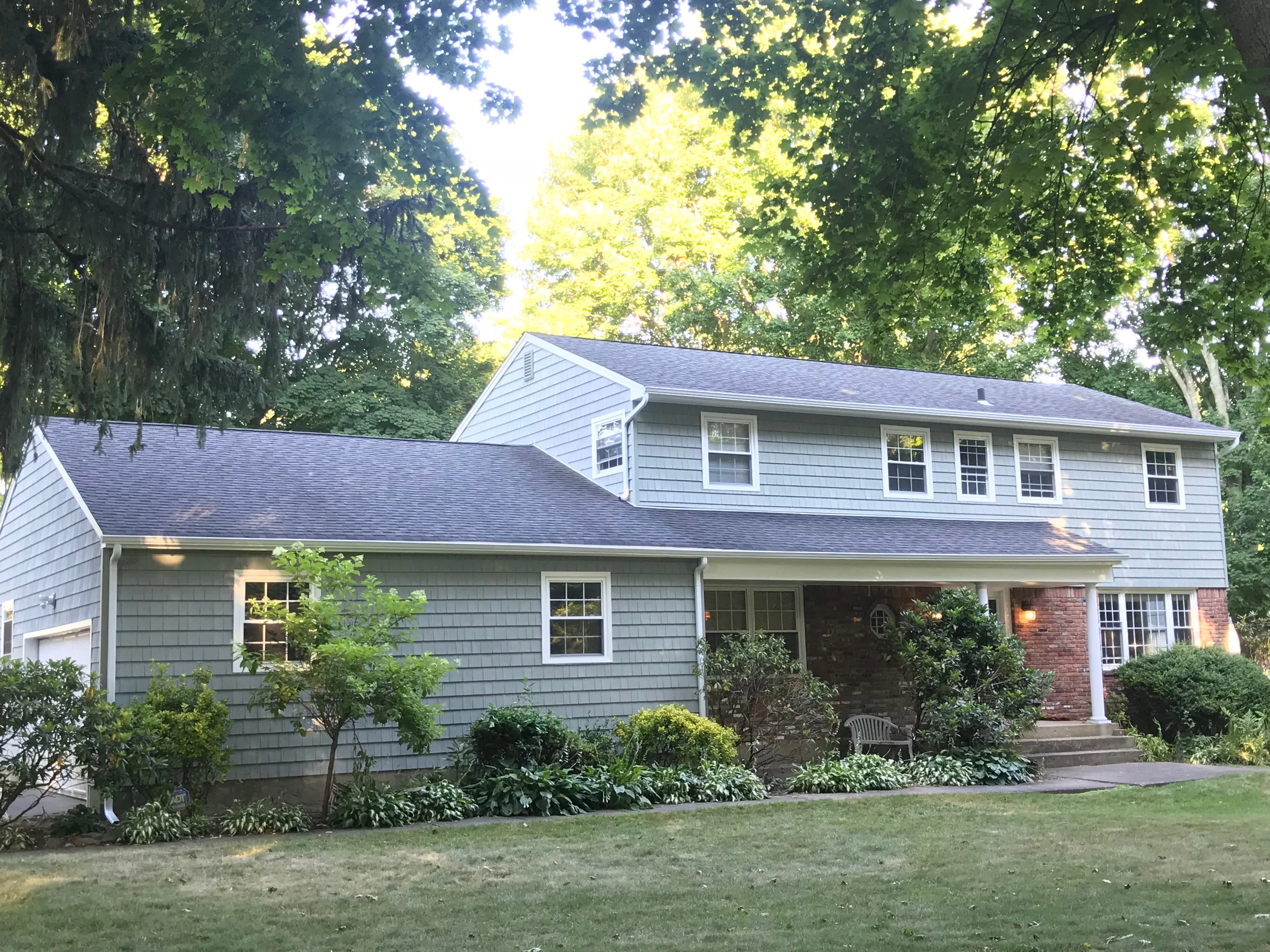 Large colonial home with light blue-gray cedar shake siding, white trim, and covered front porch
