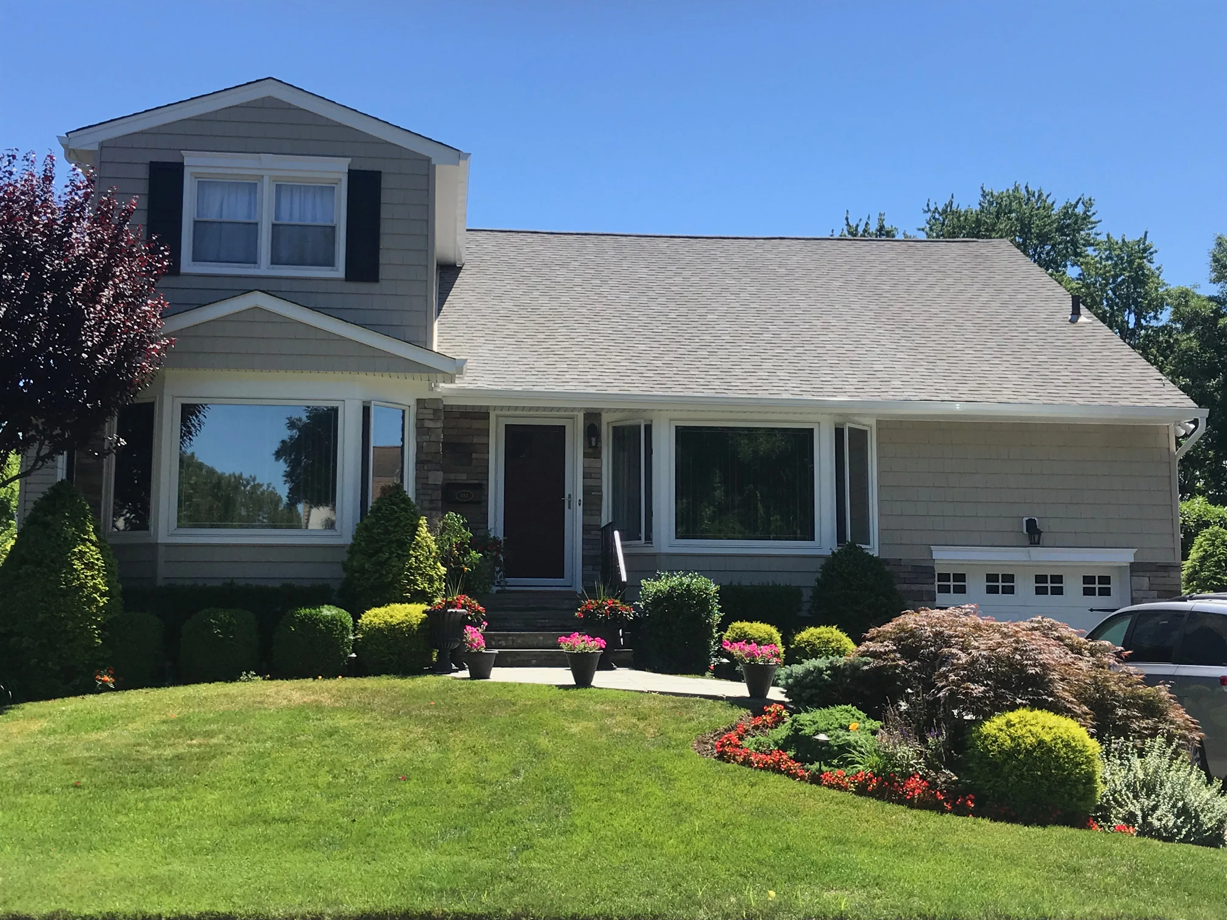 Split-level home with beige vinyl siding, black shutters, and professionally landscaped front yard