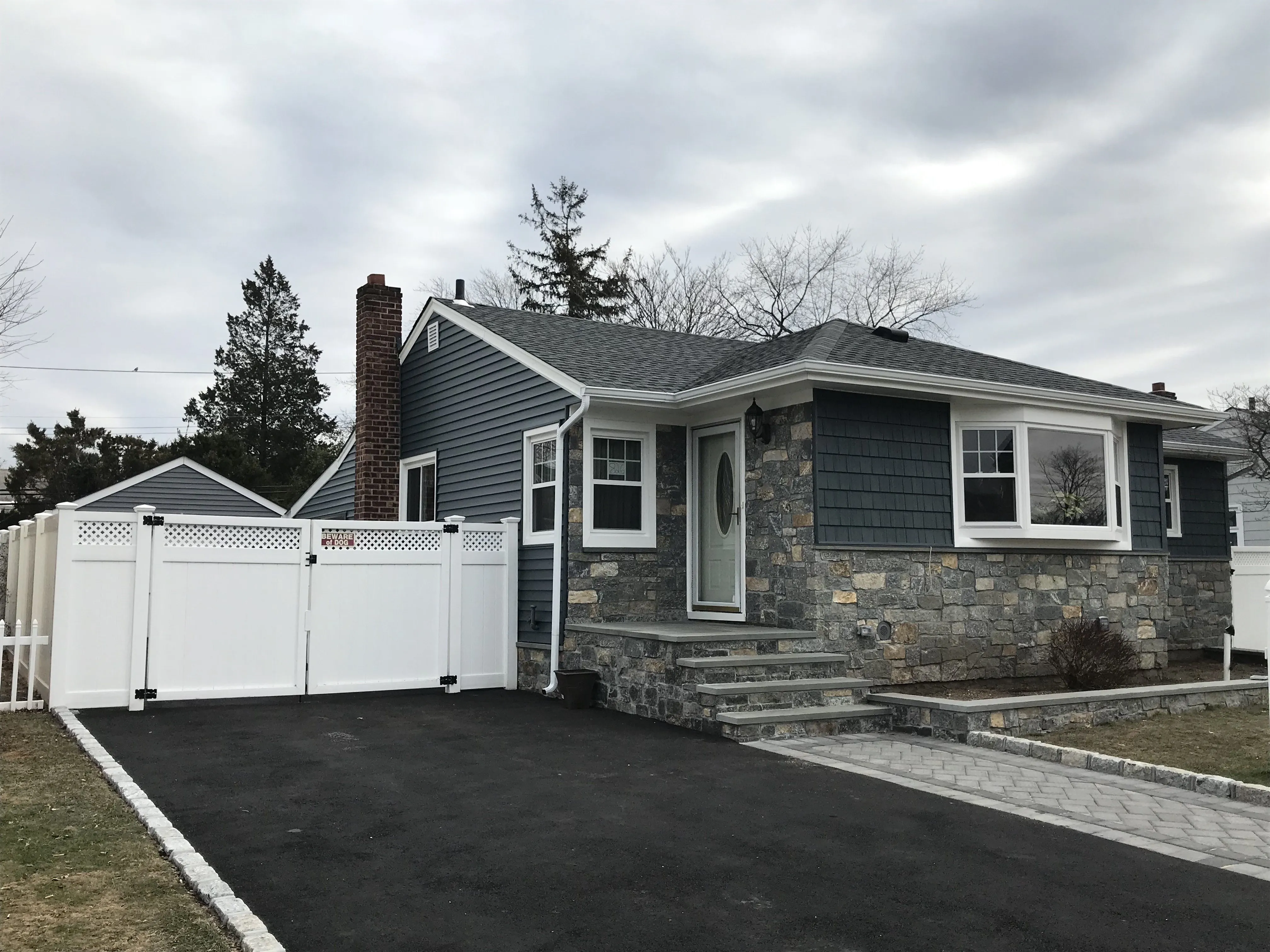 Ranch home with blue-gray vinyl siding, extensive natural stone veneer front facade, and new driveway