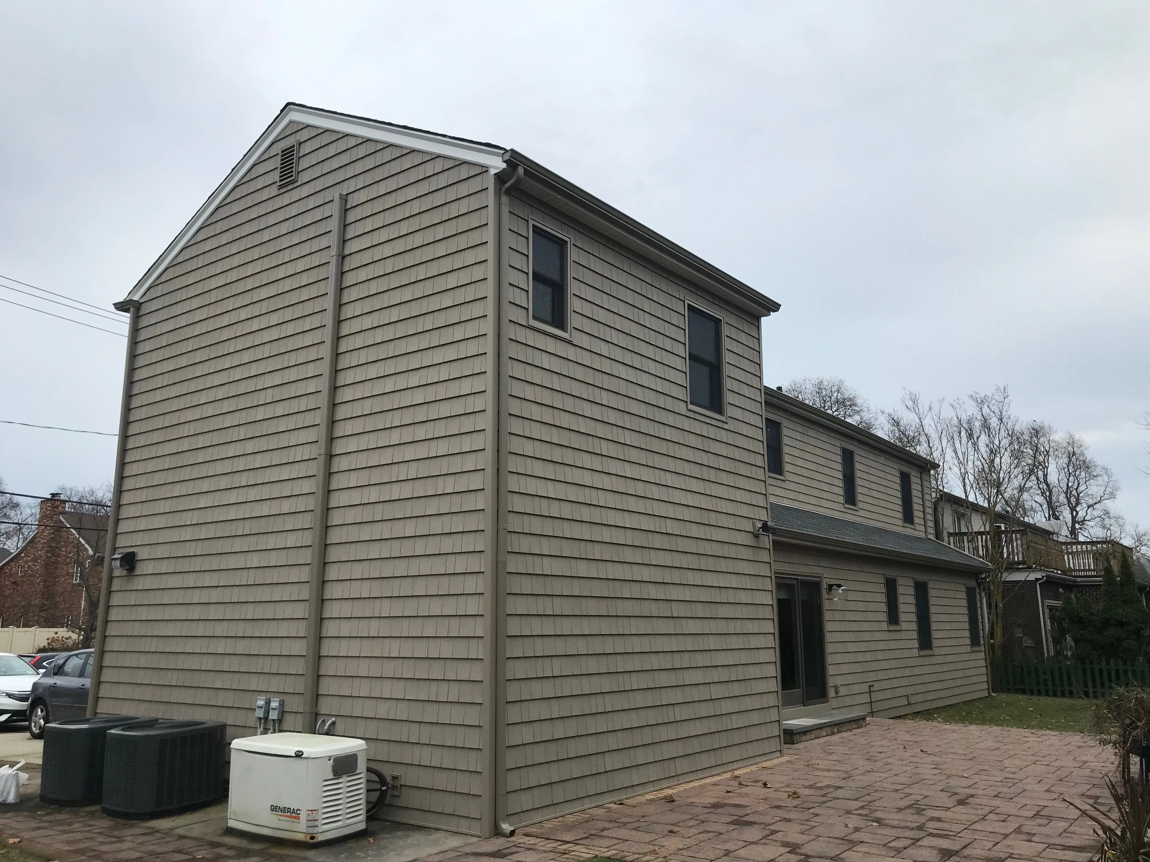 Rear view of a two-story home with tan cedar shake siding, matching gutters, and paver patio