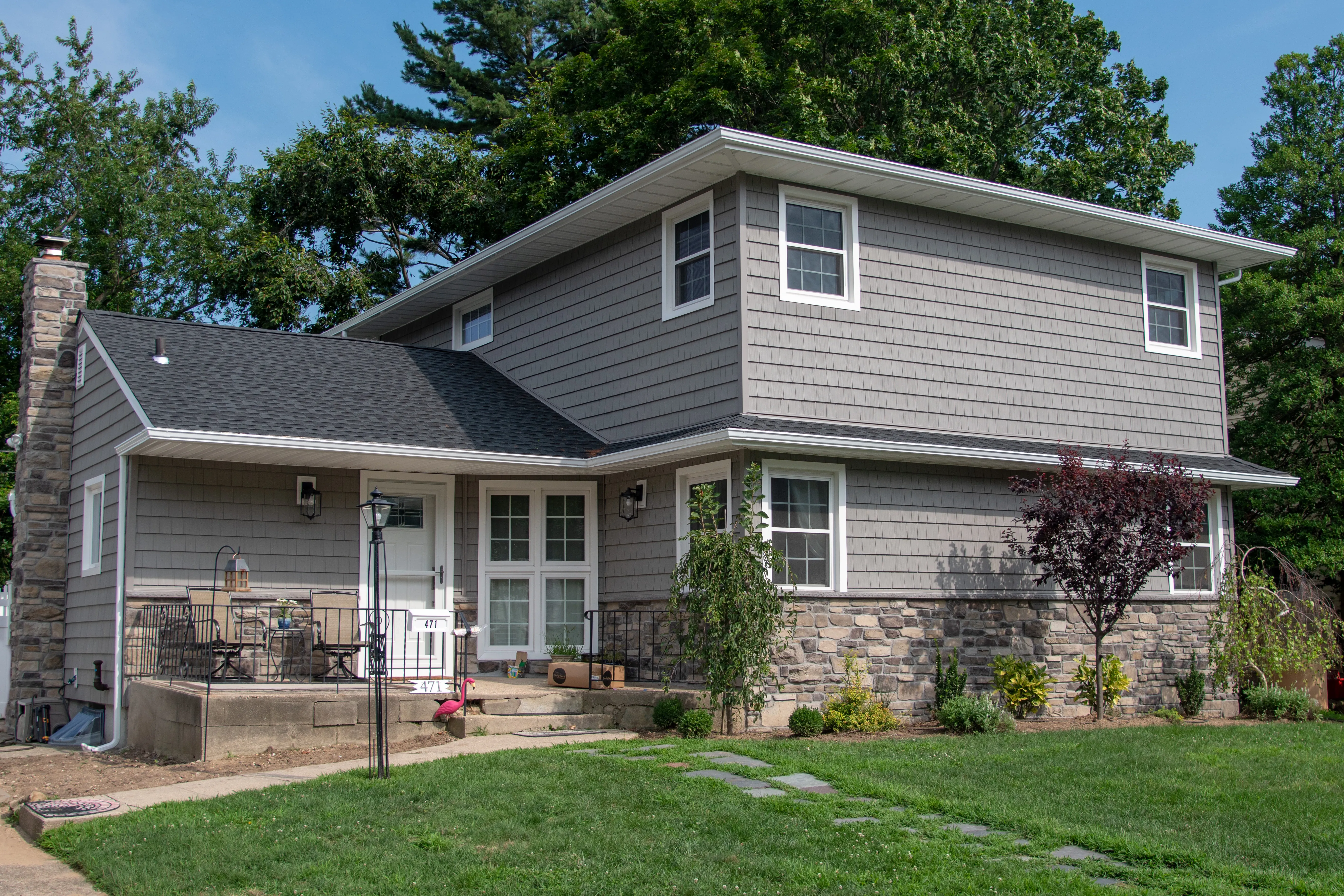 Bi-level home with gray vinyl siding, stone veneer accents on foundation and entry, and stone chimney