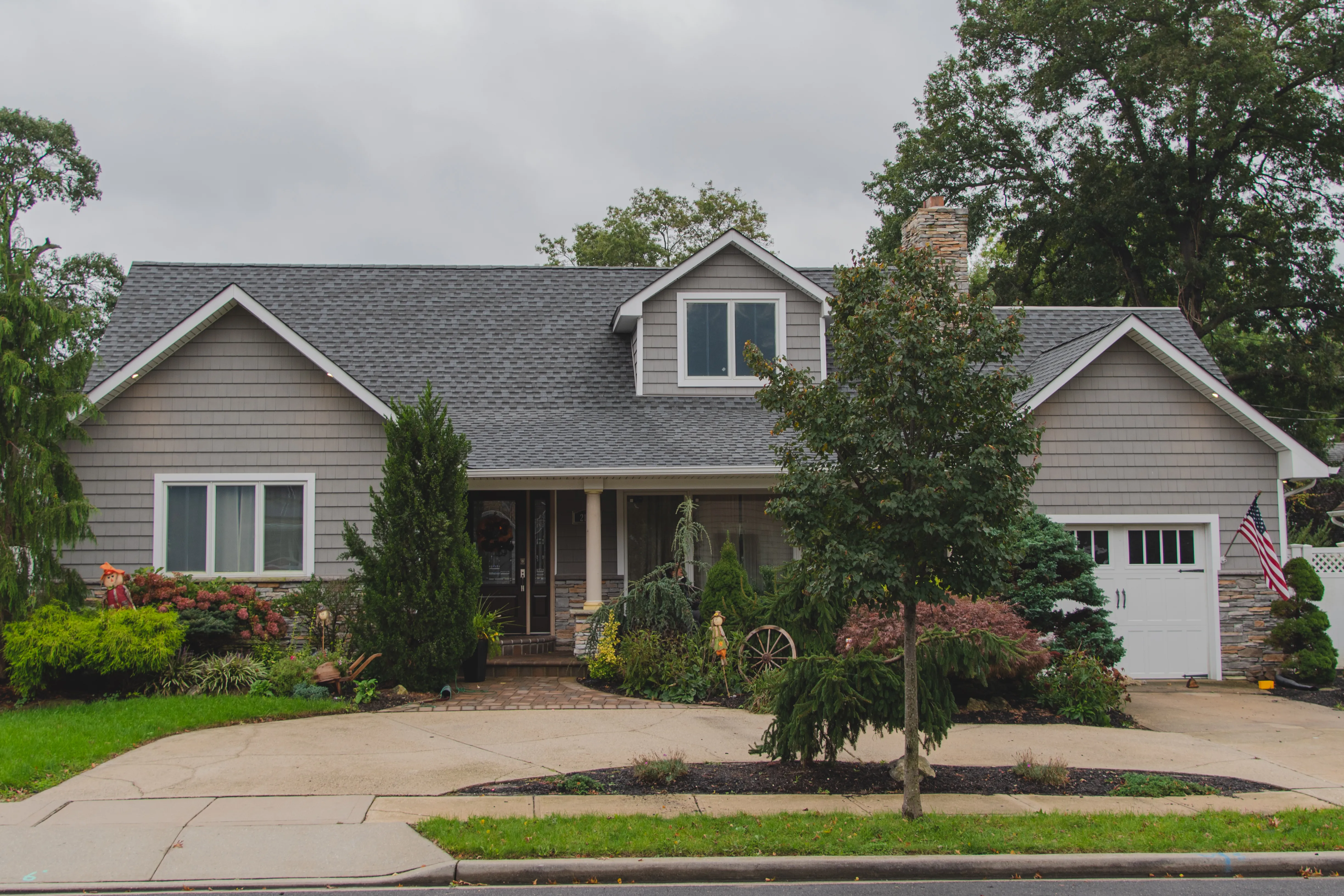 Expanded cape cod with gray vinyl siding, stone veneer on garage and foundation, and covered front porch
