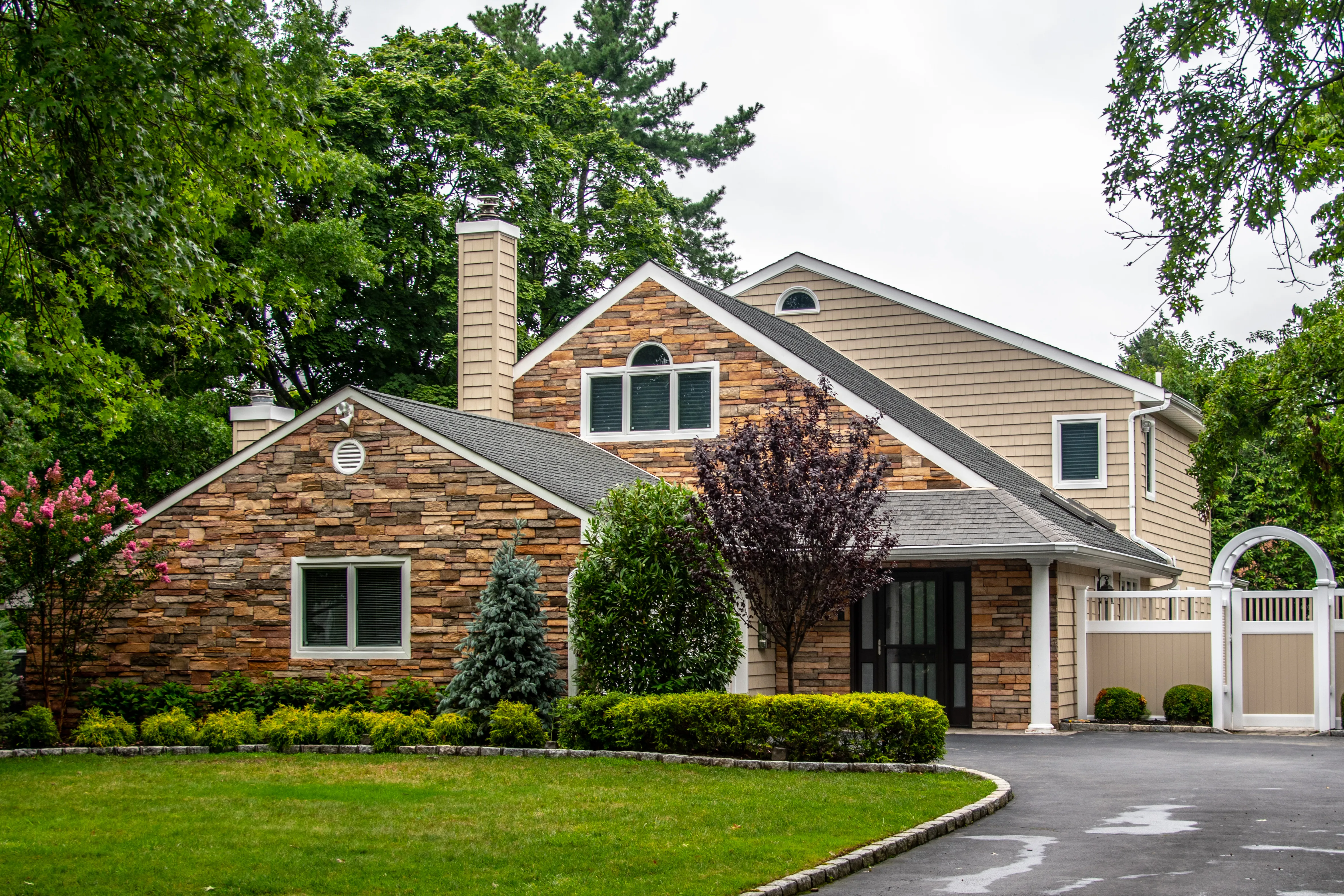 Contemporary home with extensive stacked stone veneer facade, tan vinyl siding upper level, and curved driveway
