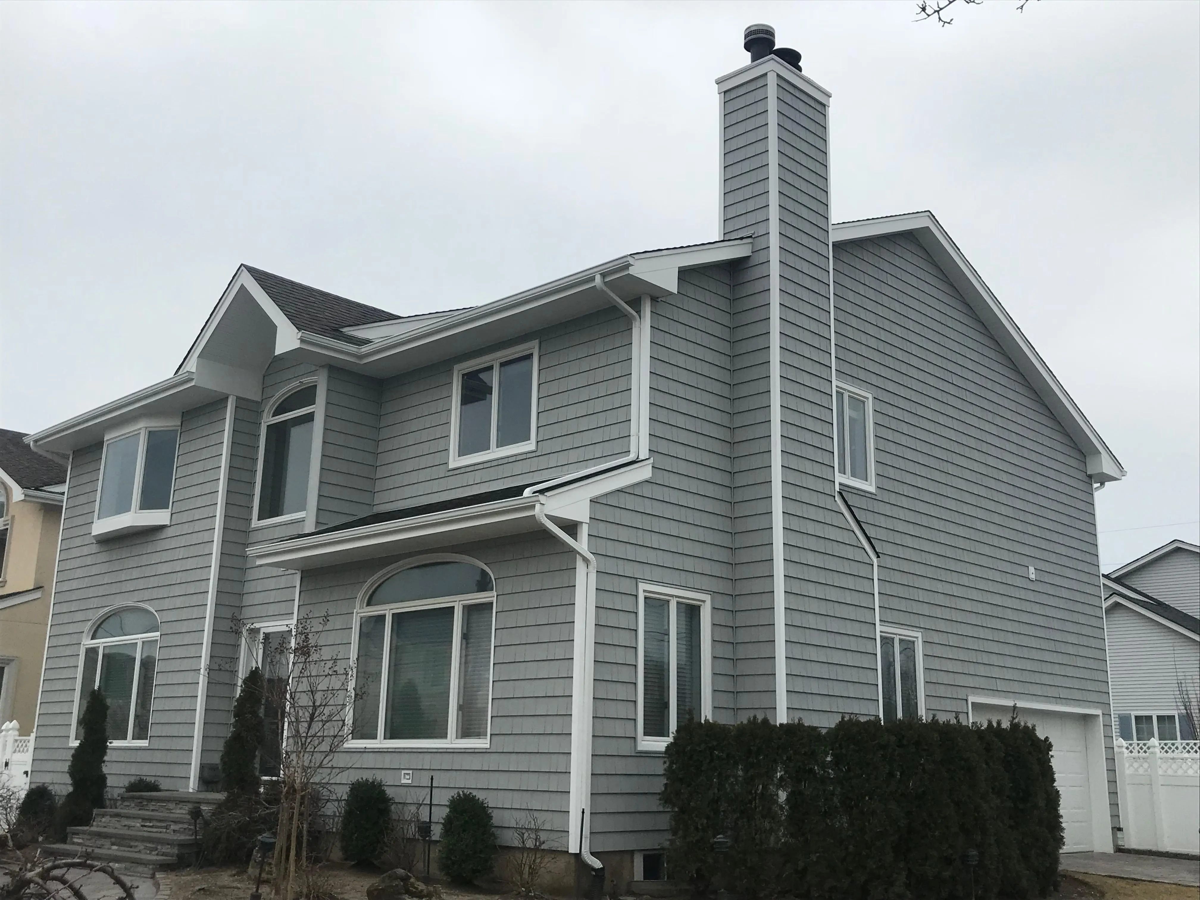 Large two-story home with gray vinyl siding, white trim, arched accent window, and stone entry steps
