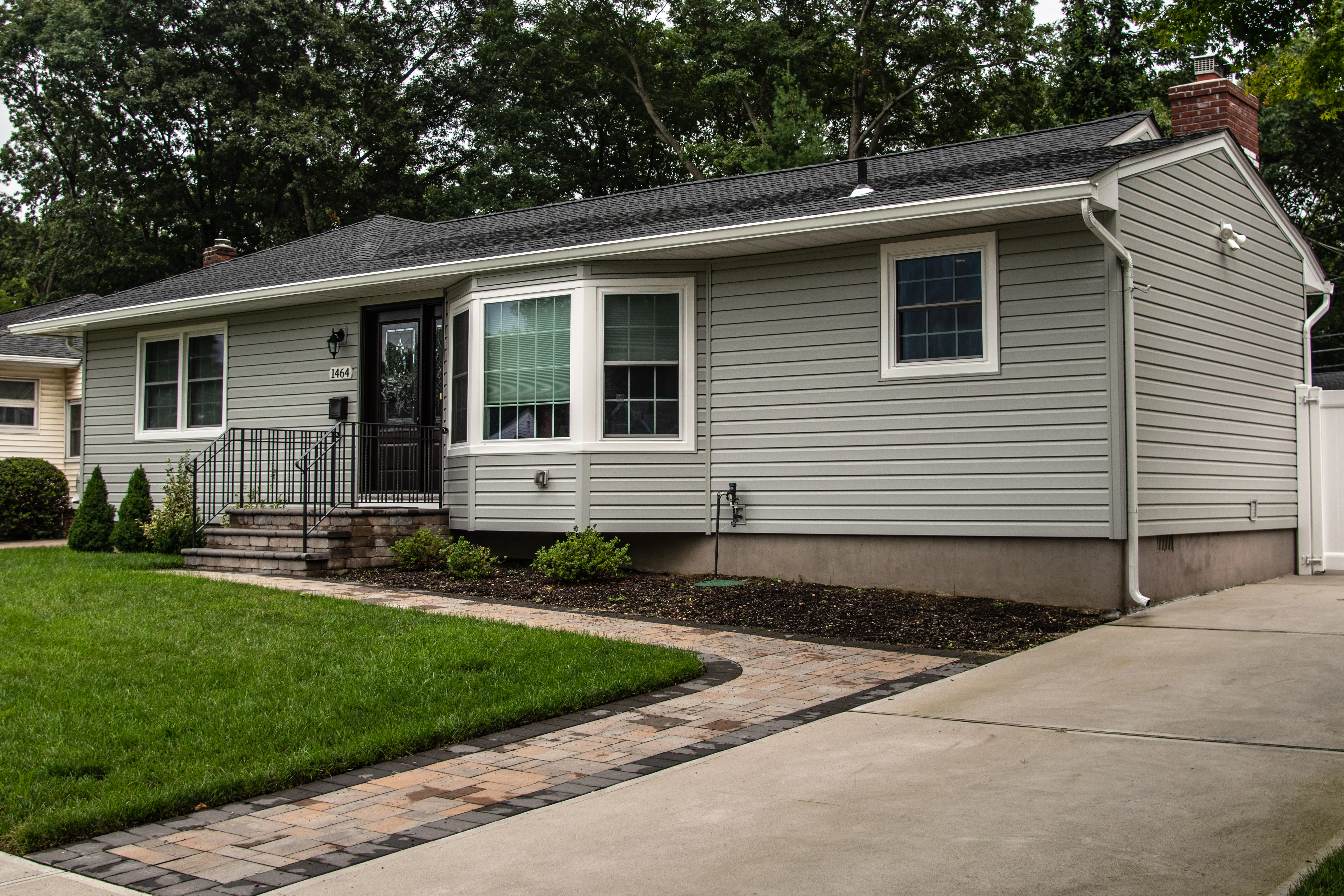 Gray horizontal vinyl siding on a ranch home with white trim, new windows, and paver walkway