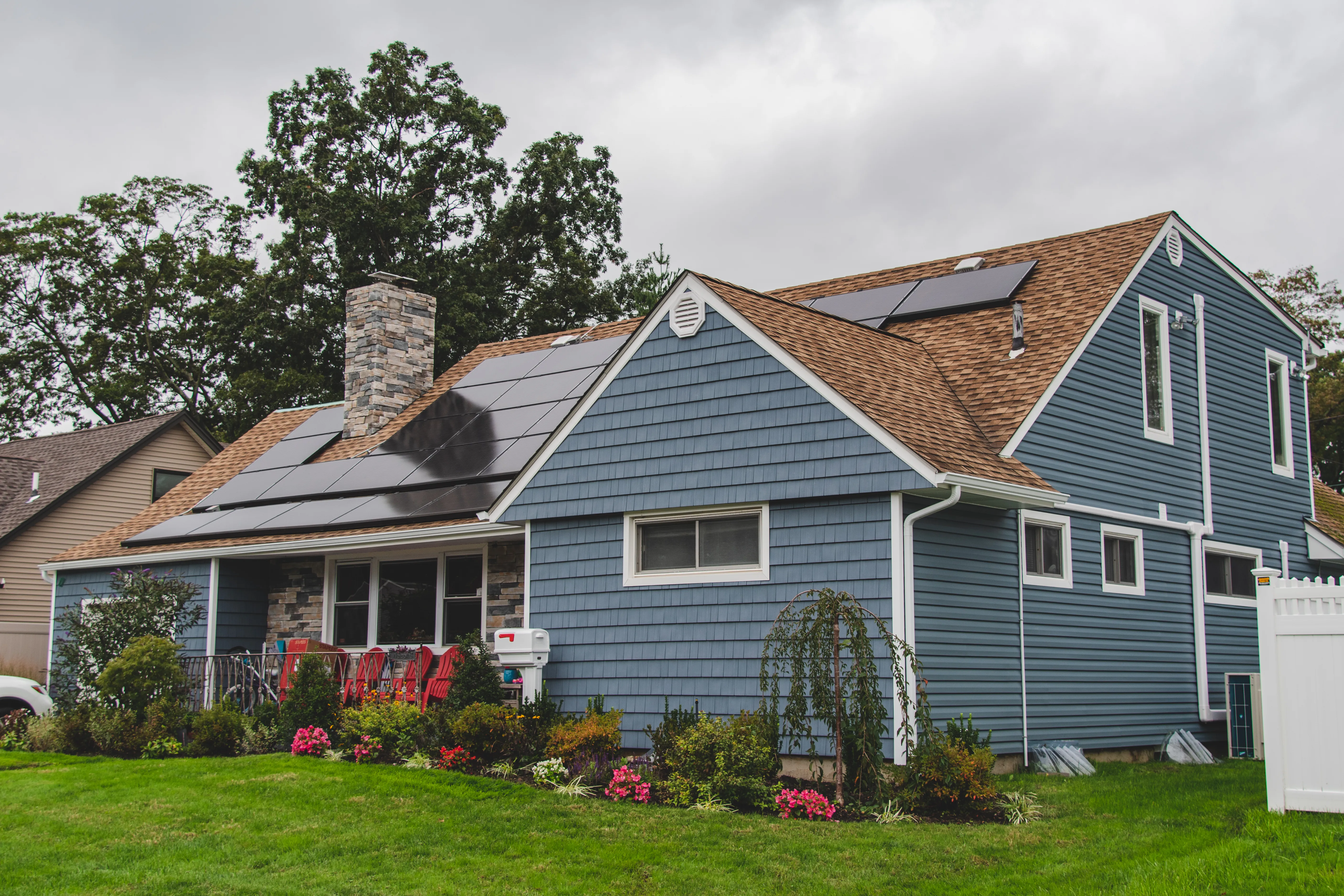 Blue cedar shake-style vinyl siding on a cape cod home with stone veneer chimney and solar panels