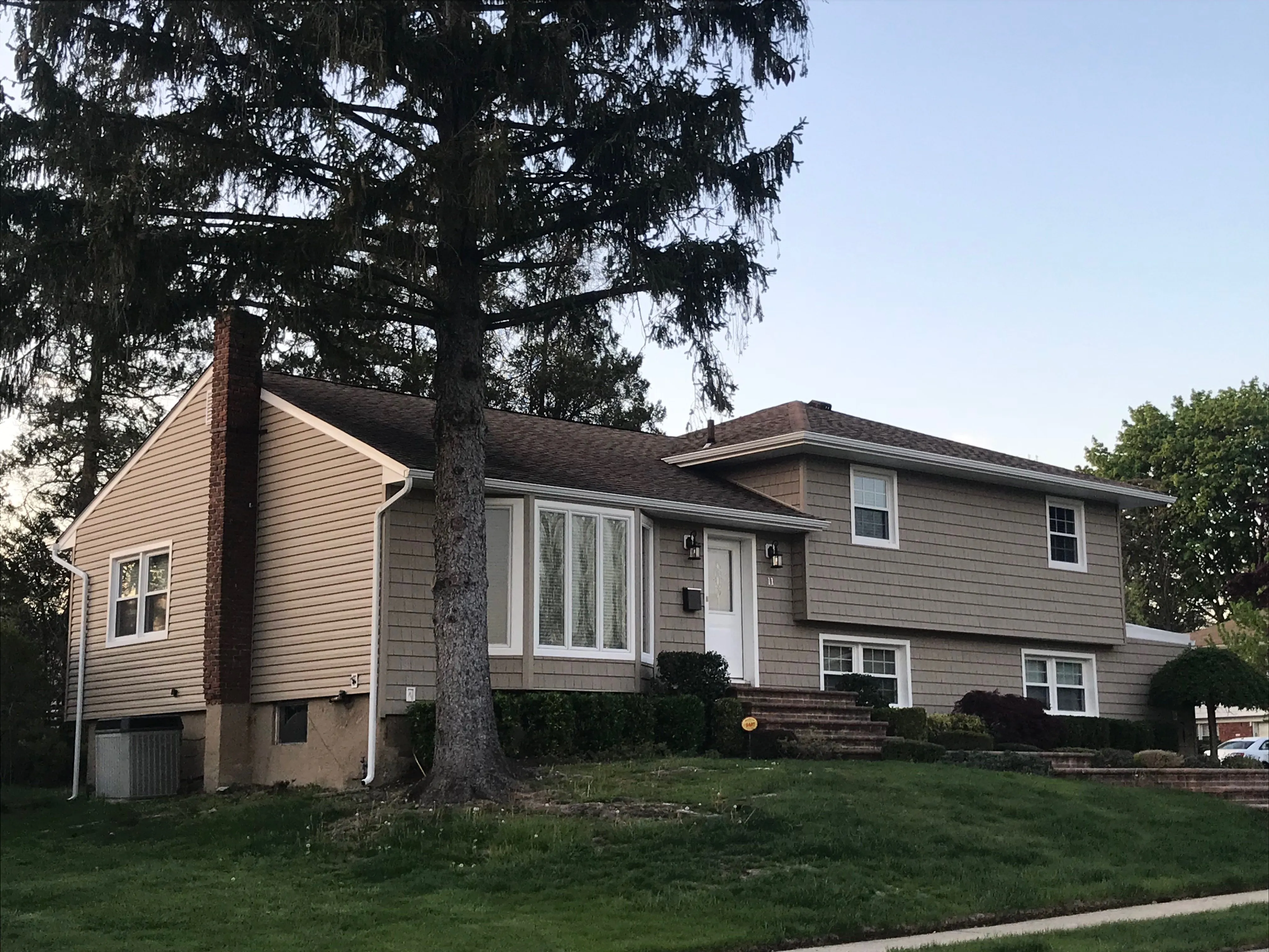 Split-level home with tan horizontal vinyl siding, white trim and windows on a corner lot
