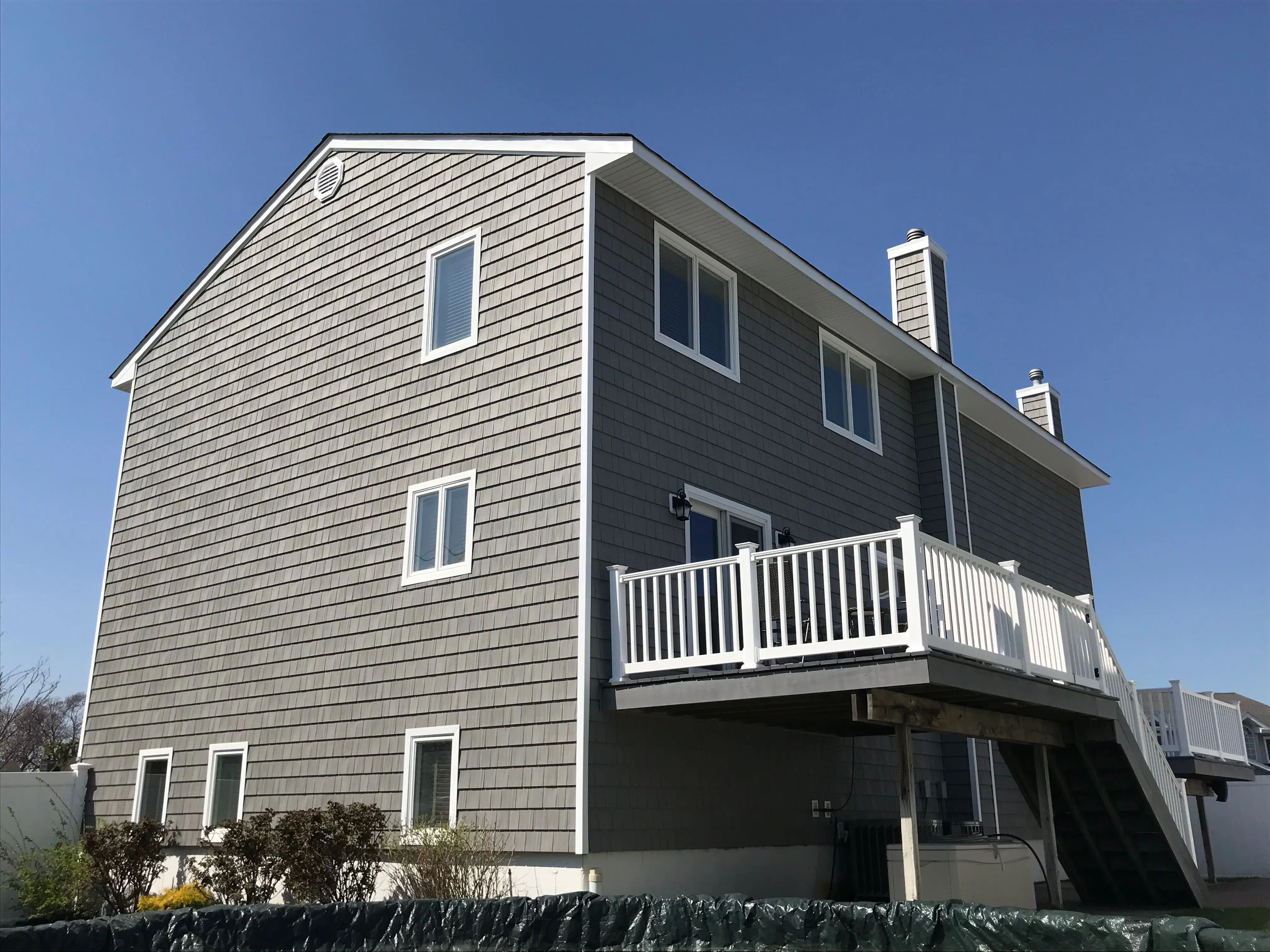Rear view of a two-story coastal home with gray cedar shake-style siding and white vinyl deck railing