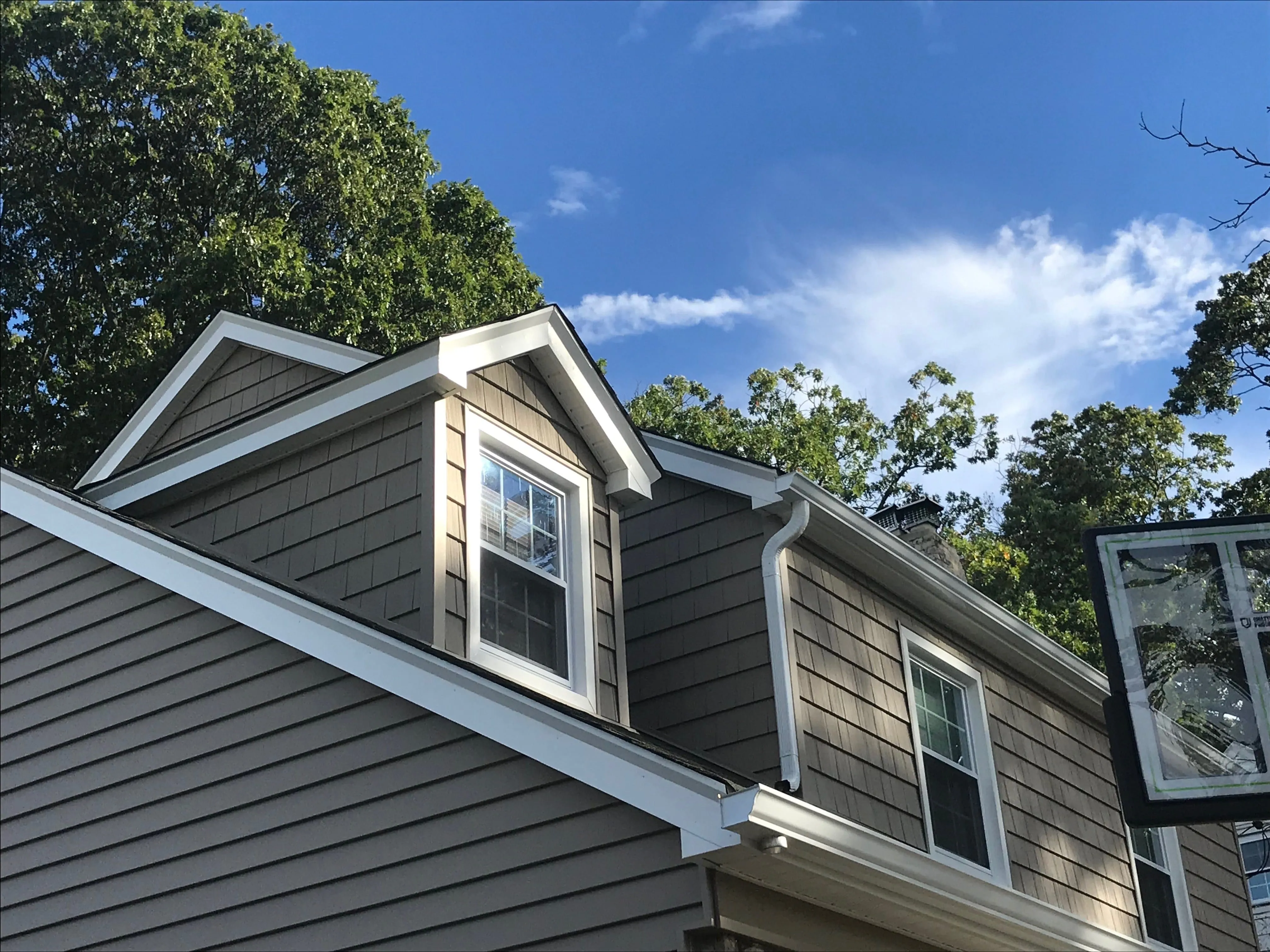 Close-up of brown cedar shake-style vinyl siding on a gable with white trim, soffit, and grid-pattern window
